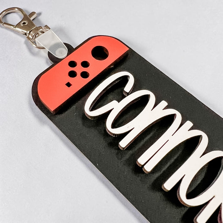 Keychain with red game controller-shaped end and 'Connor' engraving on a gray background